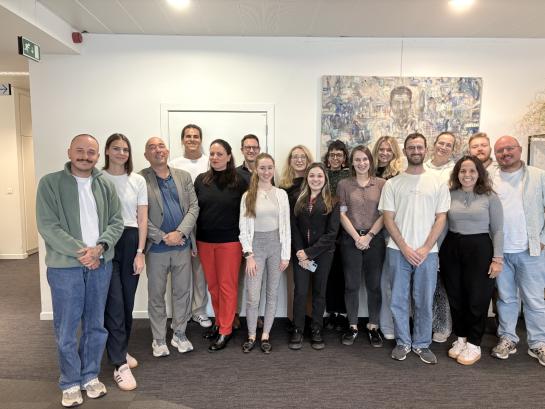 A diverse group of people posing in front of a white wall with paintings. 