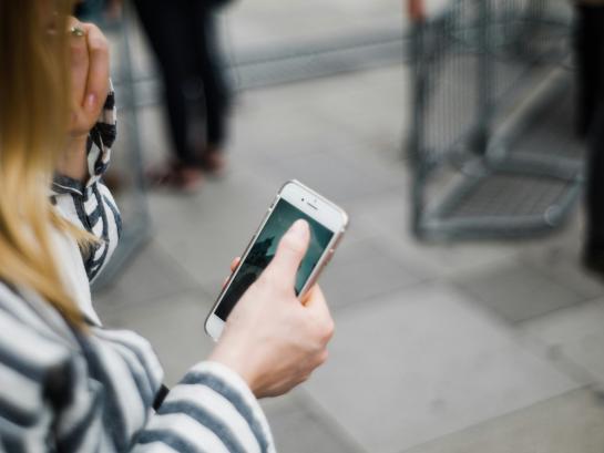 a woman or girl on her phone. She is looking at her phone while walking on the street